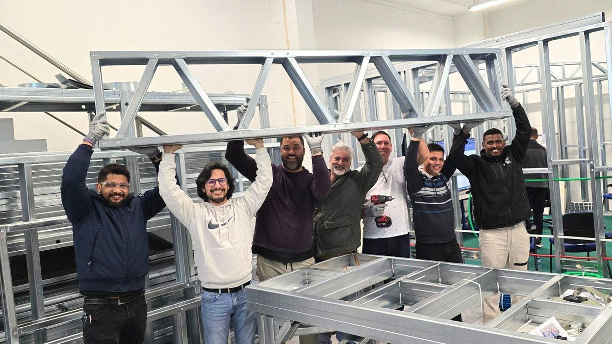Grupo de formandos a levantar em conjunto uma treliça em perfis de light steel
              frame, dentro das instalações da ConstruÁgil.